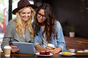 Smiling friends enjoying coffee and pastries while watching at the coffee shop