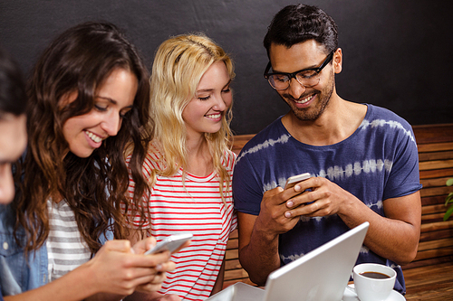 Smiling friends watching a smartphone together at the coffee shop