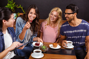 Smiling friends enjoying coffee together and using technologies