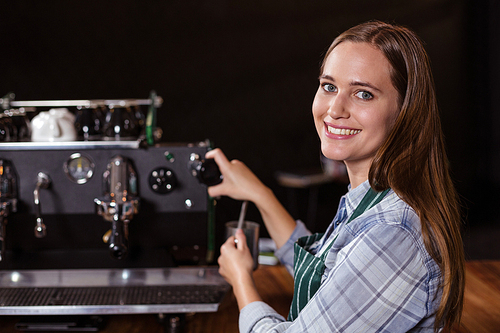 Smiling barista making hot milk with coffee machine at the bar