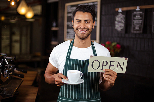 Smiling barista holding coffee and open sign in the bar