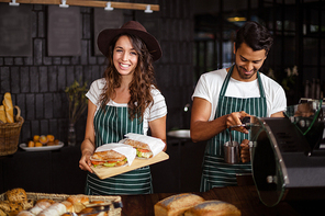 Smiling baristas holding sandwiches and making coffee in the bar