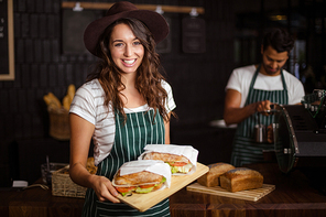 Smiling barista holding sandwiches in the bar