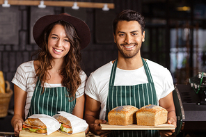 Smiling baristas holding bread and sandwiches in the bar