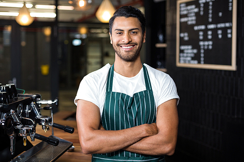 Smiling barista standing with arms crossed in the bar