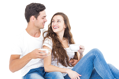 Young couple sitting on floor drinking coffee on white background