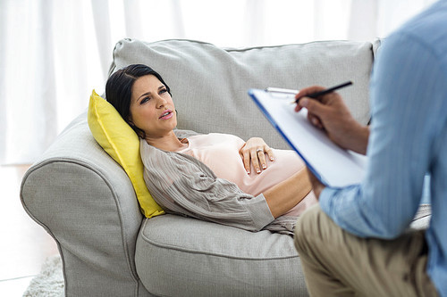 Doctor writing on clipboard while consulting pregnant woman at home