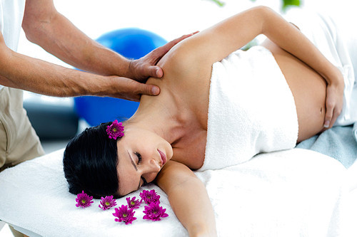 Pregnant woman receiving a back massage from masseur at health spa