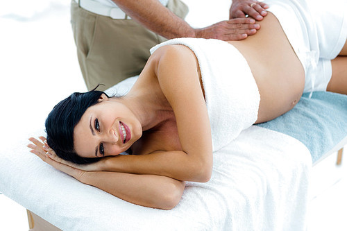 Pregnant woman receiving a back massage from masseur at home