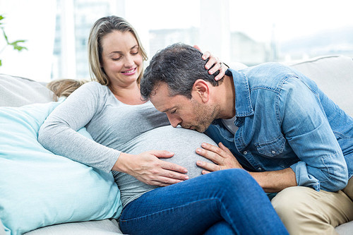 Man sitting on sofa and kissing pregnant womans stomach