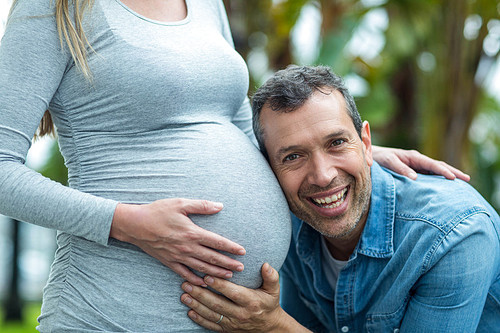 Man listening to pregnant womans stomach outdoors
