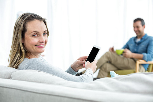 Pregnant woman sitting on sofa and using smartphone