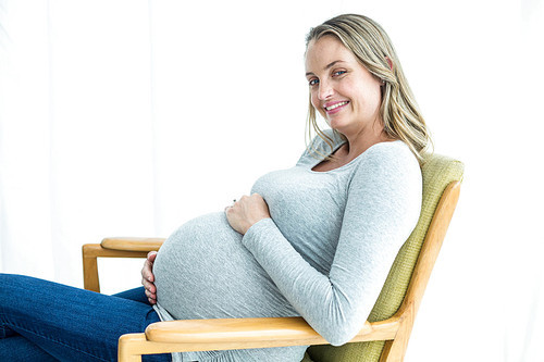 Portrait of pregnant woman sitting on chair and holding her stomach