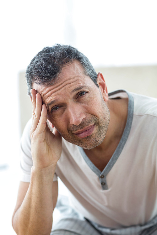 Worried man sitting on bed with hand on forehead