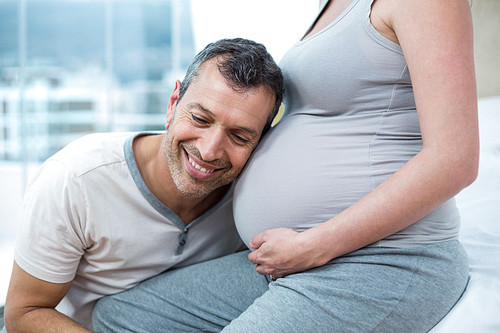 Man listening the belly of pregnant woman in their bedroom