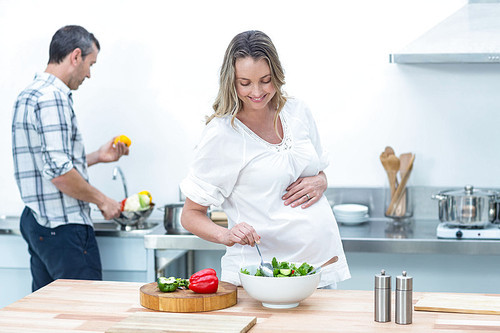 Pregnant woman making a salad in the kitchen with her partner