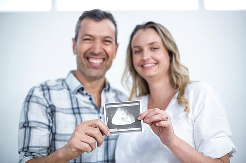 Portrait of pregnant couple holding sonography report at home