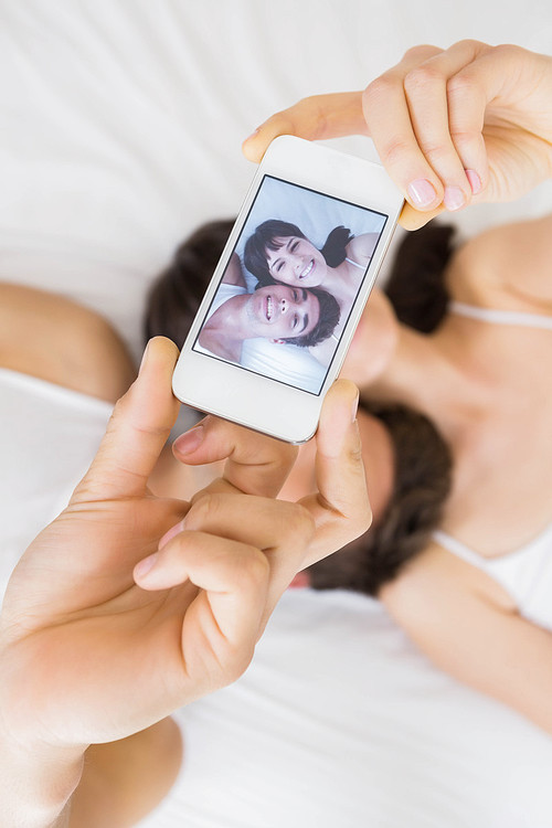Couple lying on bed and taking a selfie on mobile phone