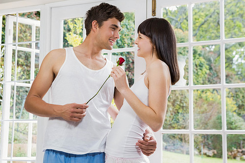 Man offering a red rose to woman in living room