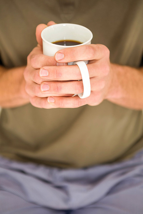 Masculine hands holding a mug of tea in the bedroom
