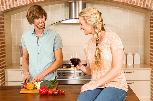 Cute couple enjoying a glass of wine and slicing vegetables in the kitchen