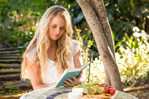 Beautiful blonde relaxing and reading with food in the garden