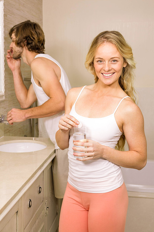 Blonde woman taking a pill with her boyfriend brushing his teeth in the bathroom at home