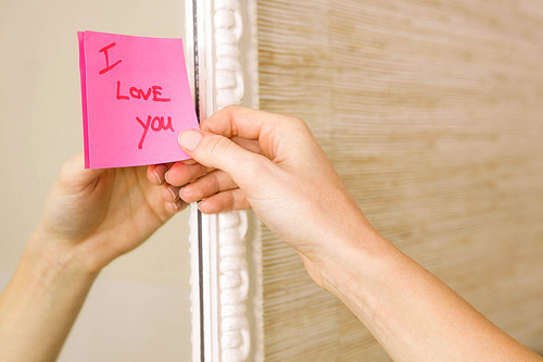 Woman sticking I love you word sticky note on mirror