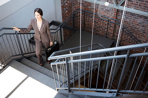 Beautiful businesswoman climbing staircase while carrying briefcase