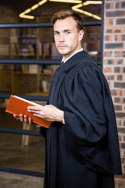 Portrait of lawyer standing near library with law book in office