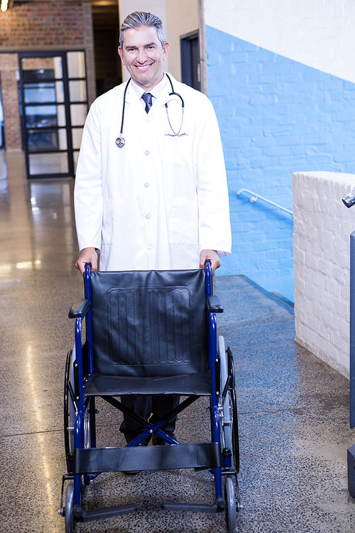 Portrait of male doctor standing with wheel chair in hospital
