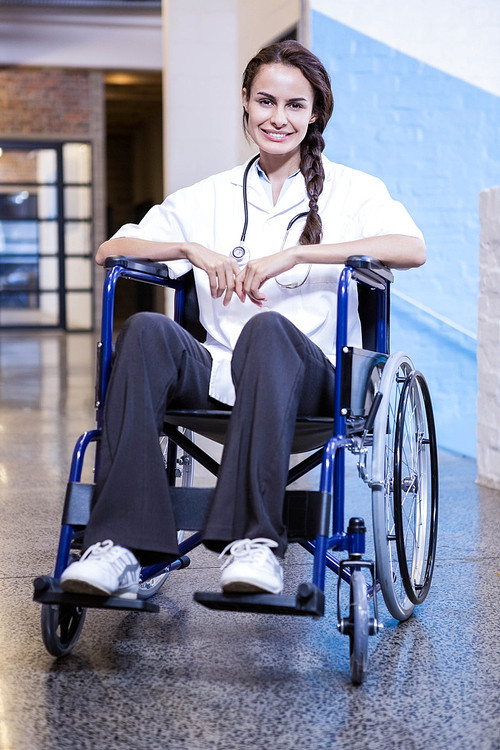 Portrait of happy female doctor sitting on wheel chair in hospital