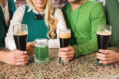 Men holding normal beers while woman holds green beer