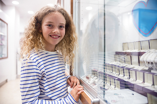 Portrait of happy girl standing near jewelry display in jewelry shop