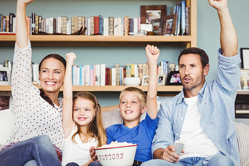 Cheerful family with arms raised while sitting on sofa at house
