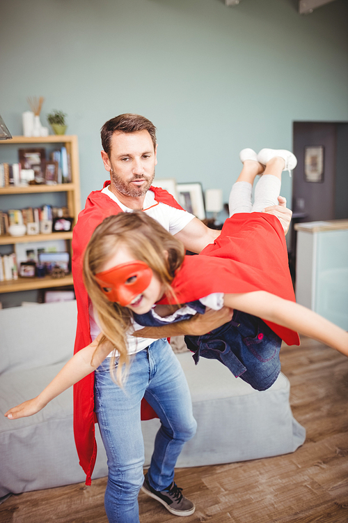 Father carrying daughter wearing superhero costume at home