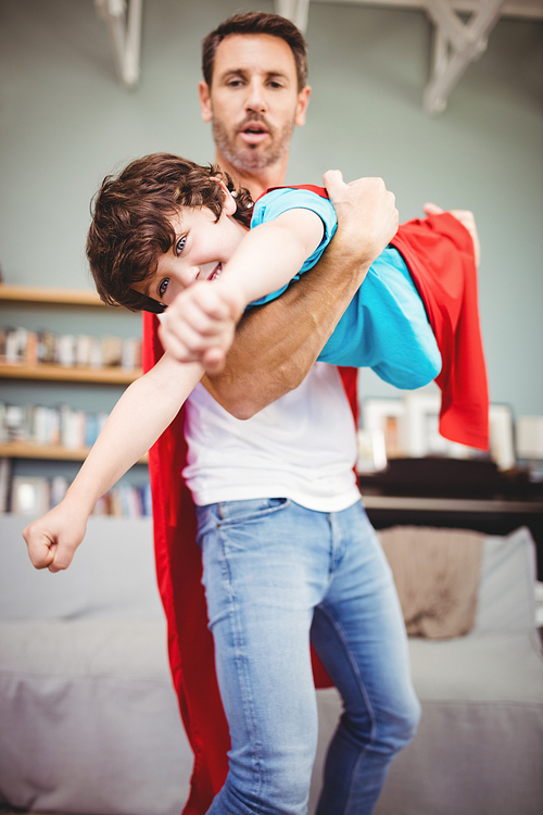 Father holding son wearing superhero costume at home