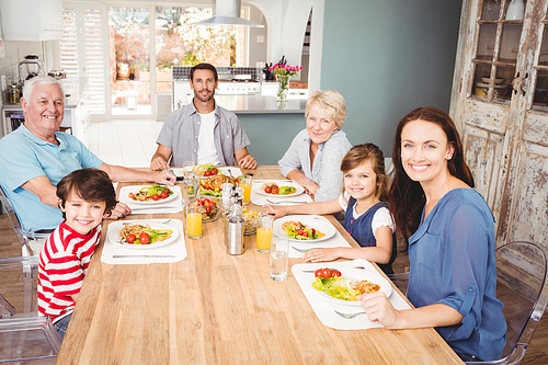 Portrait of smiling family with grandparents sitting at dining table in home