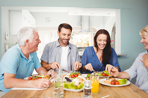 Family laughing while sitting at dining table with food in home