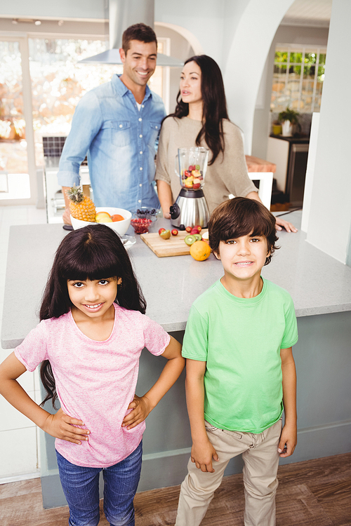 Siblings standing at table with parents preparing fruit juice in background