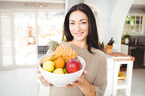 Portrait of happy woman holding fruits bowl while standing at home