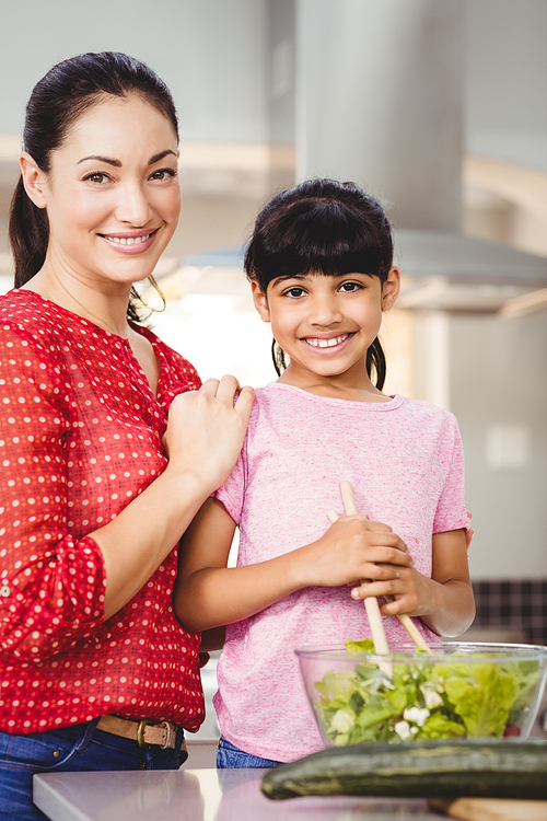 Portrait of smiling mother and daughter preparing salad at home