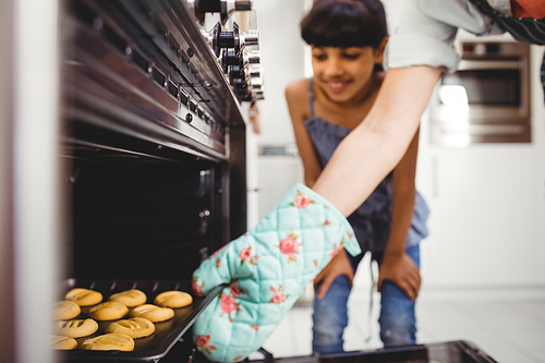 Cropped hand of woman placing cookies in oven while daughter standing in background