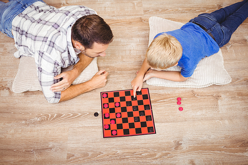 High angle view of father and son playing checker game while lying on floor at home