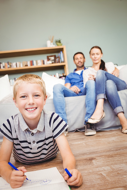 Portrait of happy boy drawing on book while parents looking at him from sofa in living room