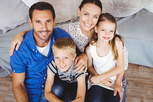 High angle portrait of cheerful family sitting by sofa in living room