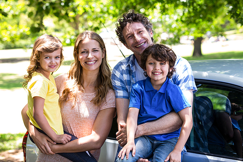 Smiling family in front of a car in the park