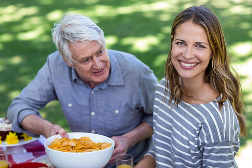 Senior man offering crisps to young woman in a park