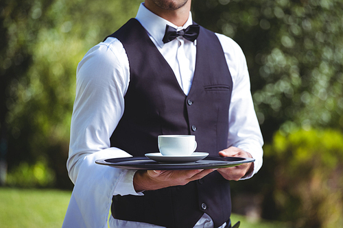 Handsome waiter holding a tray with cup of coffee outside