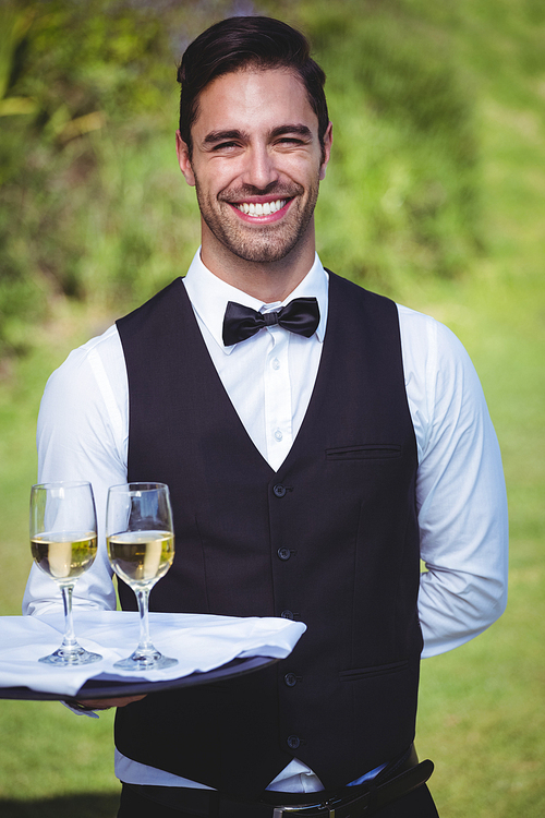 Handsome waiter holding a tray with two glasses of wine outside